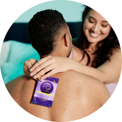 A woman smiling with her arms around a man, holding a FC2 Female Condom.